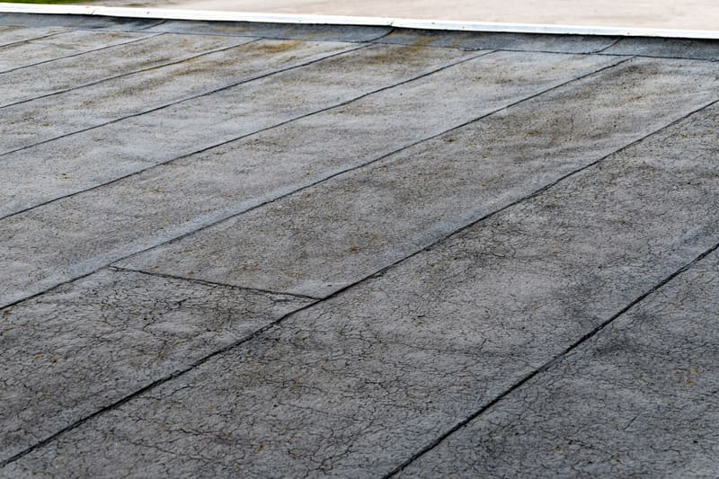 A weathered bituminous flat roof membrane, faded and crazed with fine cracks