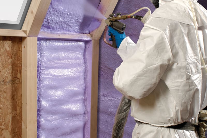 A technician in protective coveralls spraying polyurethane foam onto a framed wall